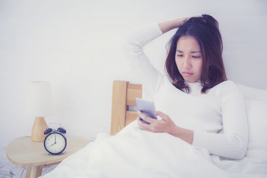 woman asian model holding a mobile phone with wake up in bedroom.