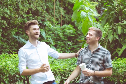 Two friends men talking standing in a garden.