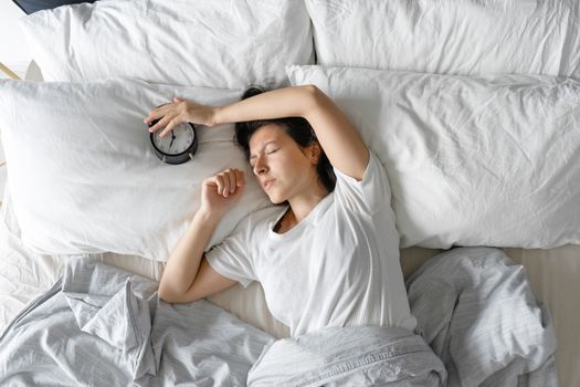 View from above. The girl sleeps next to the alarm clock. Trying to turn off the ringing alarm clock that interferes with sleep. Time to wake up. Deep sleep