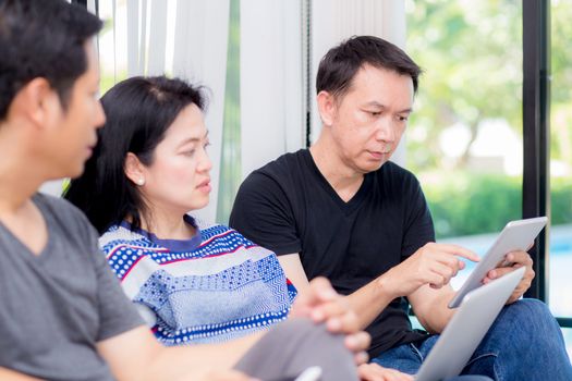 Three friends on line with multiple devices and talking sitting on a sofa in the living room in a house interior.