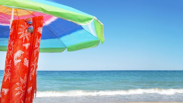 beach umbrella, pareo and sunglasses against the sea horizon and clear sky, copy space