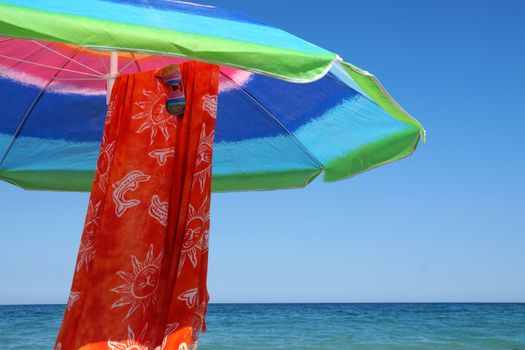 beach umbrella, pareo and sunglasses against the sea horizon and clear sky, copy space.