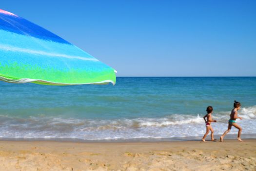 beach umbrella against the sea horizon and clear sky, children run in the background, copy space