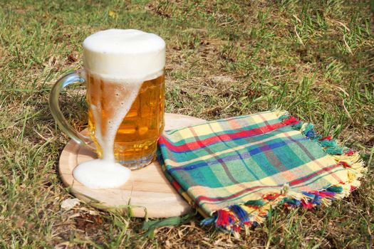 glass mug with beer and foam on a wooden tray on the grass on a sunny day