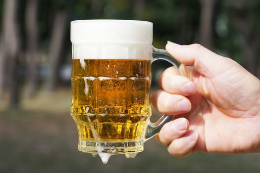 glass mug with beer and foam in a man's hand on the background of nature close up