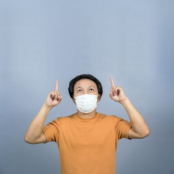 Asian man wearing face surgical mask pointing and presenting some product about coronavirus on blue color background, covid19 outbreak and pandemic,healthcare and protection against virus concept