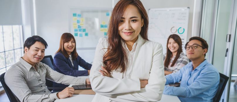 Banner of Asian Business woman with Arms Crossed and standing over the group of colleague partner when brainstorming meeting at modern workplace, human resource and small business owner concept