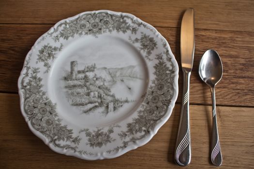 Hand-painted porcelain plate with cutlery on a massive wooden table background