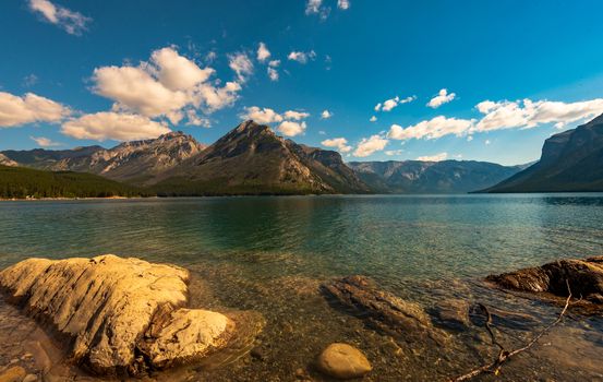 Wide angle shot of Lake Minnewanka  and the Rockies under the golden glow of the morning sun.