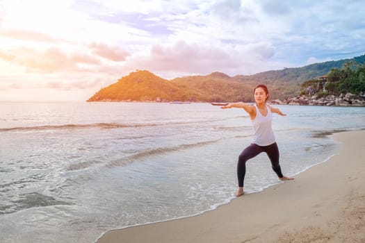 Young beautiful woman practicing yoga on the beach at sunrise