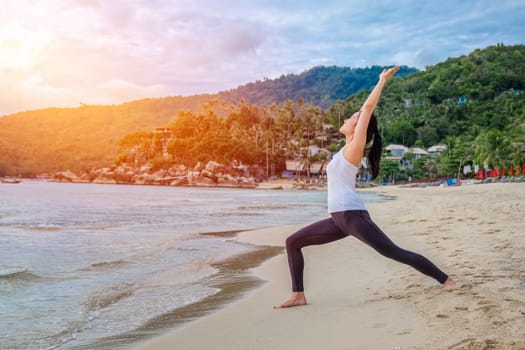Young beautiful woman practicing yoga on the beach at sunrise