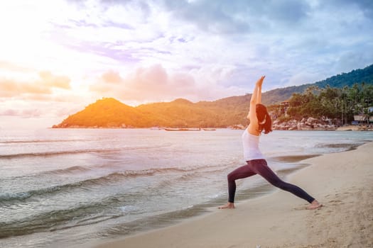 Young beautiful woman practicing yoga on the beach at sunrise