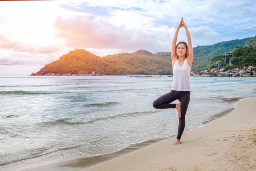 Young beautiful woman practicing yoga on the beach at sunrise

