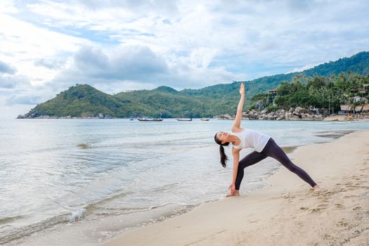 Young beautiful woman practicing yoga on the beach at sunrise