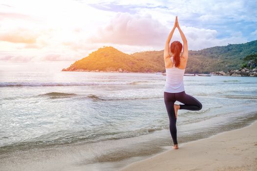 Young beautiful woman practicing yoga on the beach at sunrise