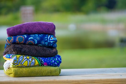 Colorful beach towels with solids and patterns stacked on a recreation table at a resort on a clear summer day