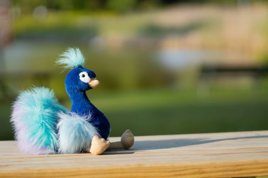 Uplifting toy plushie of a blue peacock sitting outdoors with a blurred background