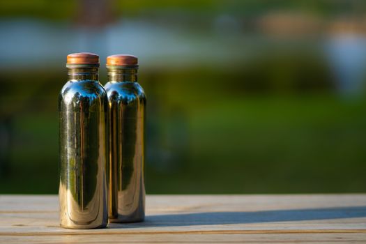 Bright pair of copper water bottles sitting on a picnic table during camping trip