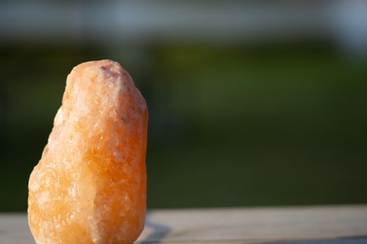 Blurred outdoor background with a closeup of a himalayan salt rock on a wood table in the summer sunlight