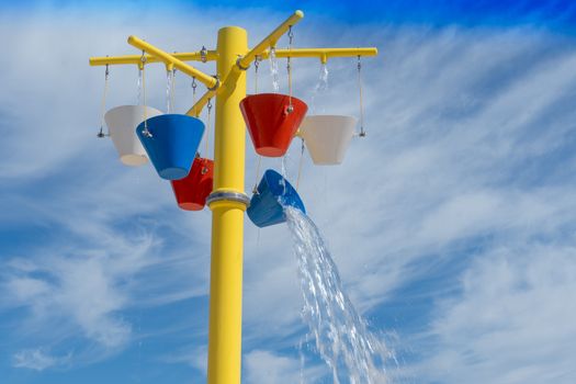 Colorful buckets of water pouring on a splashpad in the summer sun