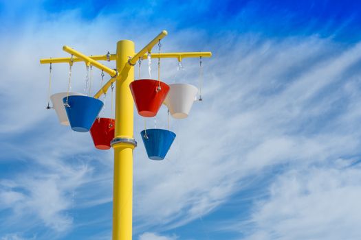 Colorful buckets of water pouring filling up on a cloud background and waiting to spill on a splashpad in the summer