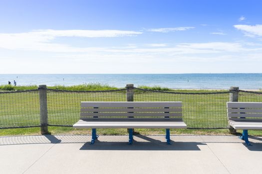 Lone park bench in front of a Michigan beach with sunlight grass and sand in the distance