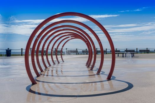 Red spray tunnel shotting water on the splashpad in the summer sun with the lake in the distance