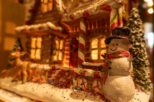 Closeup of a happy snowman in front of a colorful gingerbread house