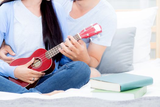 Young Asian couple playing ukulele relaxing with happiness and joyful in bedroom.