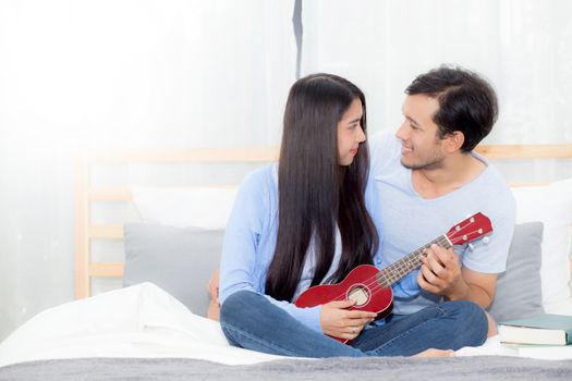 Young Asian couple playing ukulele relaxing with happiness and joyful in bedroom.