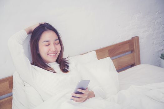 woman asian model holding a mobile phone with wake up in bedroom.