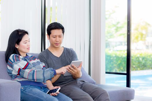 Two friends on line with multiple devices and talking sitting on a sofa in the living room in a house interior, communication concept.