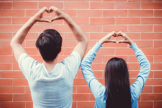 Young asian couple happy in love with gesture hand heart shape on brick background.