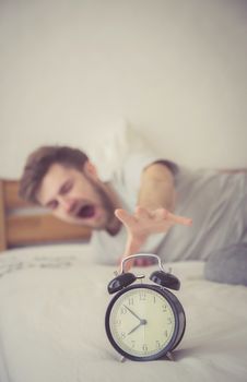 man sleepy nationality american reaching for the alarm clock sleeping on bedroom.