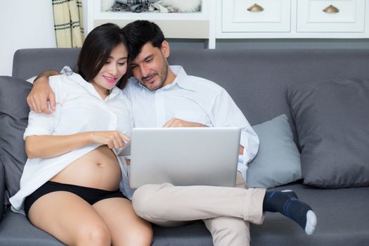 Portrait of a asian young couple husband and wife sitting on the sofa while using notebook computer in living room.