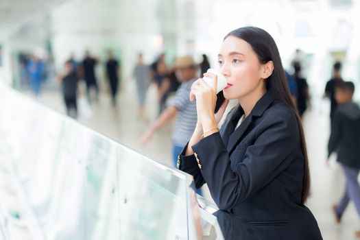 Asian businesswoman talking mobile phone and holding a coffee cup against urban scene, business concept.