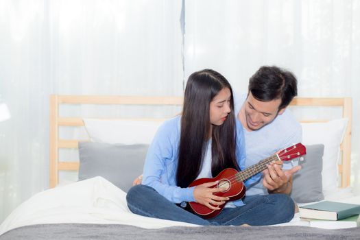 Young Asian couple playing ukulele relaxing with happiness and joyful in bedroom.