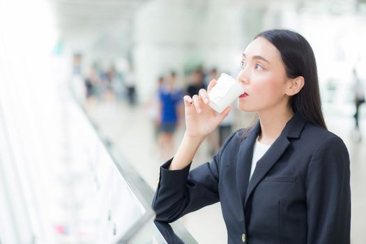 Asian businesswoman talking mobile phone and holding a coffee cup against urban scene, business concept.