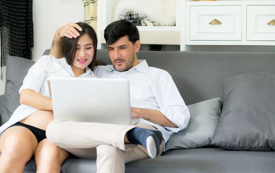 Portrait of a asian young couple husband and wife sitting on the sofa while using notebook computer in living room.