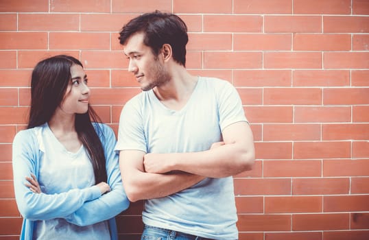 Young couple asian attractive looking face and smiling while standing back to back against brick wall with romantic.