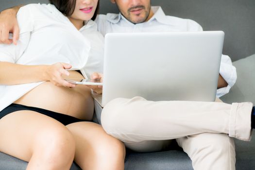 Portrait of a asian young couple husband and wife sitting on the sofa while using notebook computer in living room.