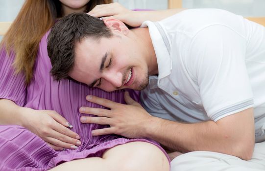Beautiful pregnant asian woman and husband listening to baby with belly in bedroom with happiness, family concept.