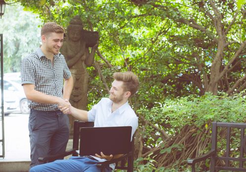 Two american business people working of the notebook computer and handshake glad success at outdoor.