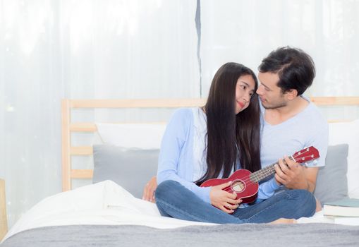 Young Asian couple playing ukulele relaxing with happiness and joyful in bedroom.