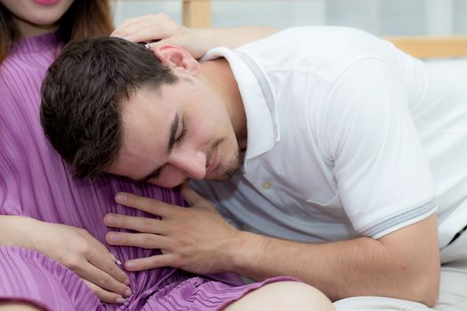 Beautiful pregnant asian woman and husband listening to baby with belly in bedroom with happiness, family concept.