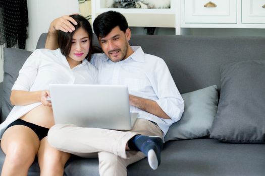 Portrait of a asian young couple husband and wife sitting on the sofa while using notebook computer in living room.