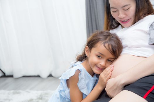 Little child listening baby in belly and hug mother with happiness in room.