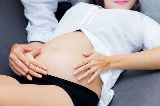 Pregnant Mother and father sitting hugging holding belly on sofa, family concept.