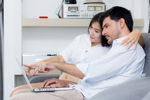 Portrait of a asian young couple husband and wife sitting on the sofa while using notebook computer in living room.