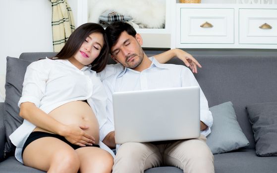 Portrait of a asian young couple husband and wife sitting on the sofa while using notebook computer in living room.